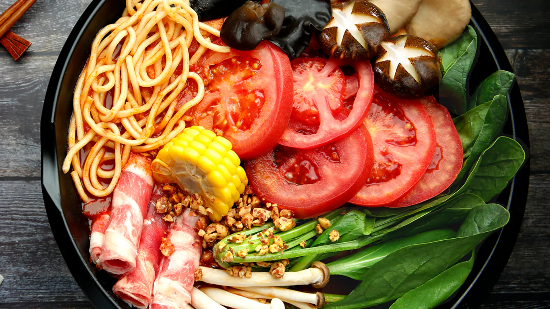 Super Meat Combo features a bowl of spicy broth - based hot pot with noodles, assorted meats like beef rolls, vegetables such as tomatoes, corn, mushrooms, and green beans, garnished with crushed nuts at YGF Malatang, a Chinese restaurant in Daly City